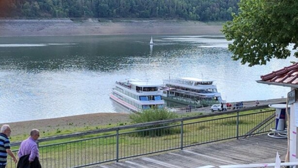 Eine Holzterrasse mit Picknicktischen mit Blick auf einen See und ein Boot.