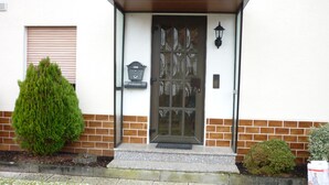Ein Haus mit Haustür, Briefkasten und einem kleinen Garten mit zwei Büschen.