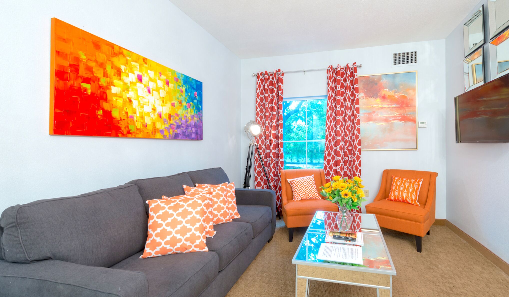 A living room with a grey sofa, orange armchairs, a coffee table, and a colorful abstract painting.
