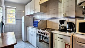 A compact kitchen with white cabinets, a stove, a microwave, and a coffee maker.