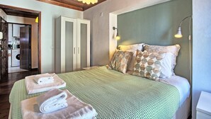 A bedroom with a bed, pillows, a bedside lamp, and a view of a kitchen area.