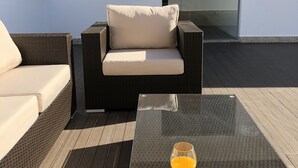 A modern outdoor seating area with a wicker sofa and a glass table with a drink. - Casa Jerónimo B&B (Lamego)
