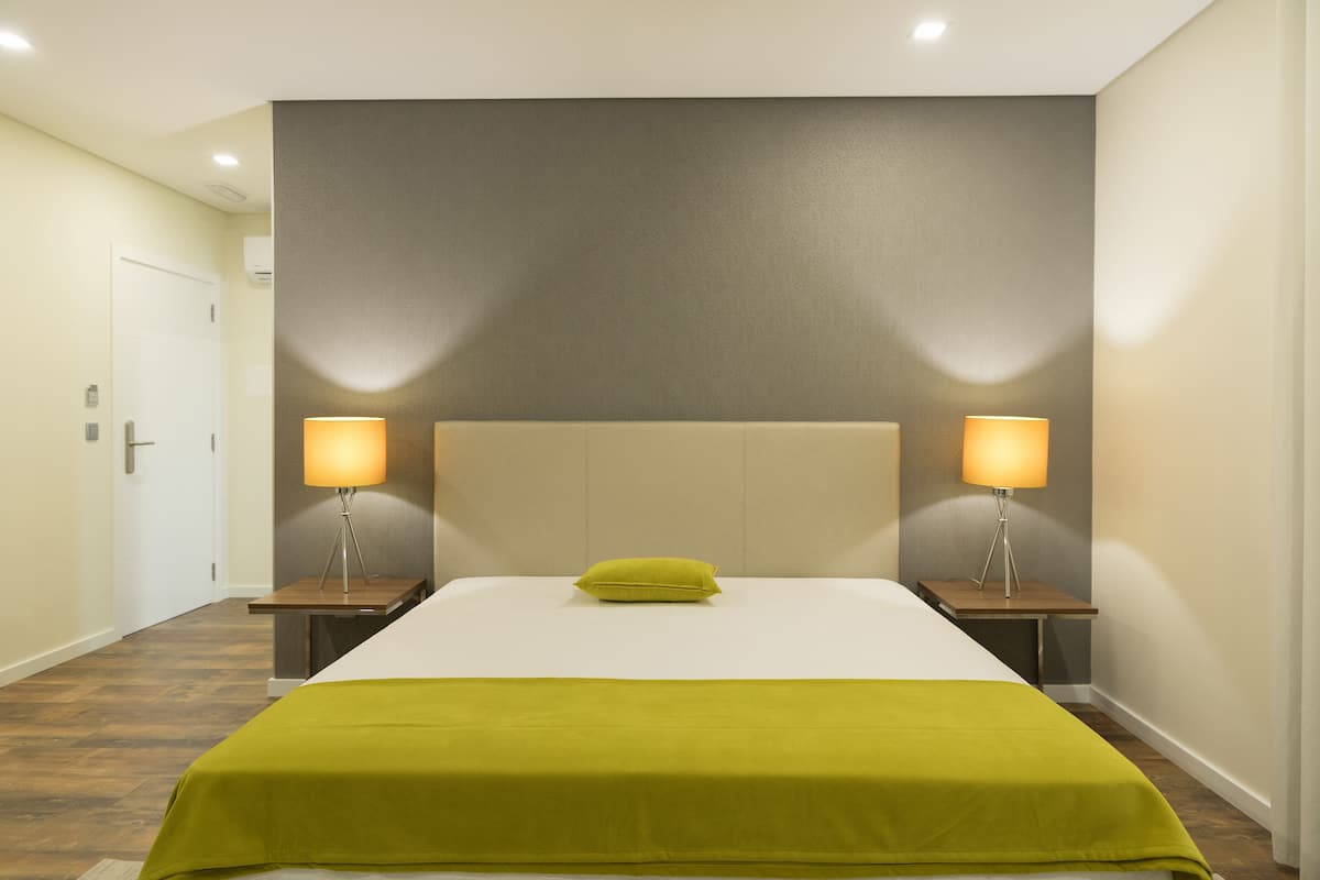 A hotel room with a large bed, two bedside lamps, a pillow, and a wooden nightstand.