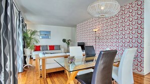 Un salon moderne avec une table à manger en verre, un canapé et un mur décoré d’un motif.
