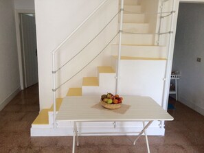 Una escalera con barandilla blanca y una mesa con cesta de fruta al pie.