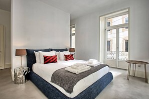 Habitación de hotel moderna con una cama grande, una mesita auxiliar y un balcón con vistas a la ciudad.