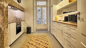 A narrow kitchen with white cabinets, a microwave, and a window with a view of a snowy landscape. - MyPlace - Lisbon - Luxury Trindade (Lisboa)