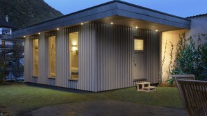 Un bâtiment moderne, de plain-pied, doté de grandes fenêtres et d’un toit plat, situé dans un espace verdoyant avec une montagne en arrière-plan.