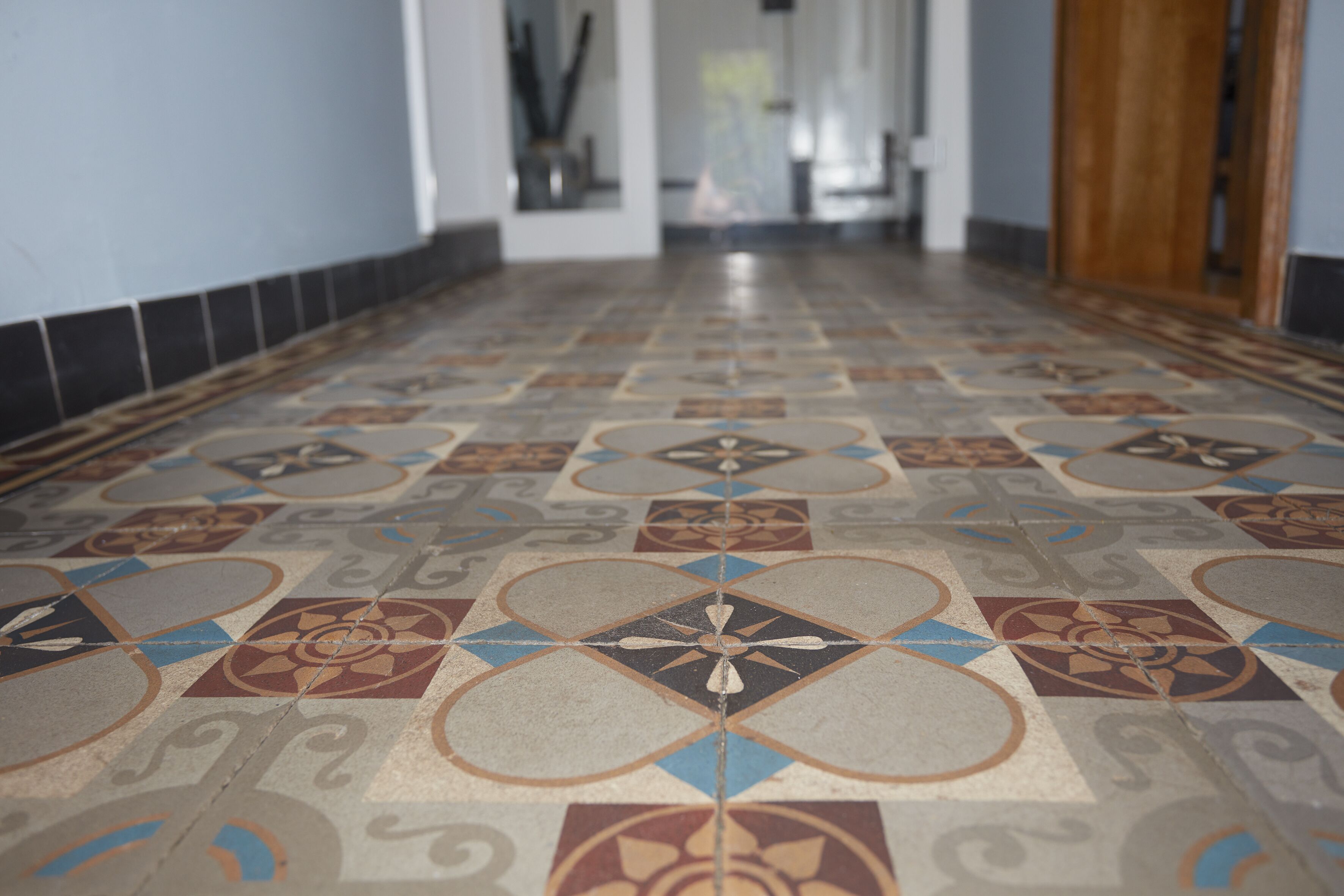 A hallway with patterned floor tiles and a wooden door on the right.