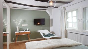 A bedroom with a bed, a desk, a chair, a TV, and a window.