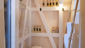 Une petite pièce en bois, avec un plafond en pente, des étagères remplies de bouteilles, une échelle et un tabouret moelleux.