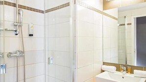Een moderne badkamer met een douche met glazen wand, een witte wastafel en een spiegel erboven.