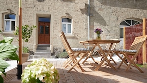 A wooden deck with a table and chairs, a door, and a stone building in the background. - Ferienhaus Lemon Tree (Rieden)