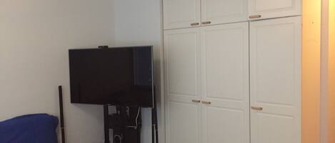 A room with a television, a blue couch, and a white wardrobe.