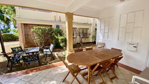 A covered patio area with a wooden table and chairs, a small garden, and a view of the surrounding greenery. - ❤️ All on foot | Family villa 8 pers facing the beach | Gold Coast (FLIC EN FLAC)
