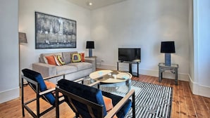 A modern living room with a sofa, two armchairs, a coffee table, a TV, and a painting on the wall.