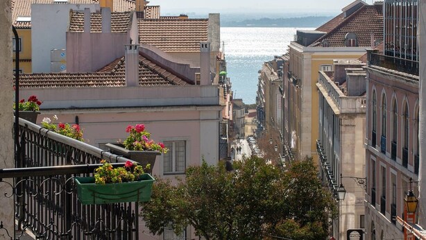 A view of a city street with buildings and a body of water in the distance.
