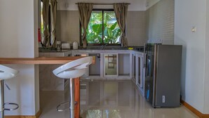 A modern kitchen with a central island, white cabinets, a stainless steel refrigerator, and a window with curtains.