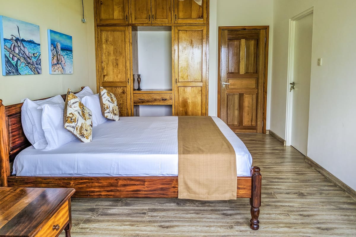 A bedroom with a wooden bed, a nightstand, a dresser, and a wardrobe. There are two paintings on the wall.