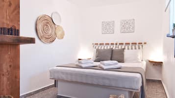 A bedroom with a bed, bedside tables, a wooden shelf, a woven rug, and a basket.