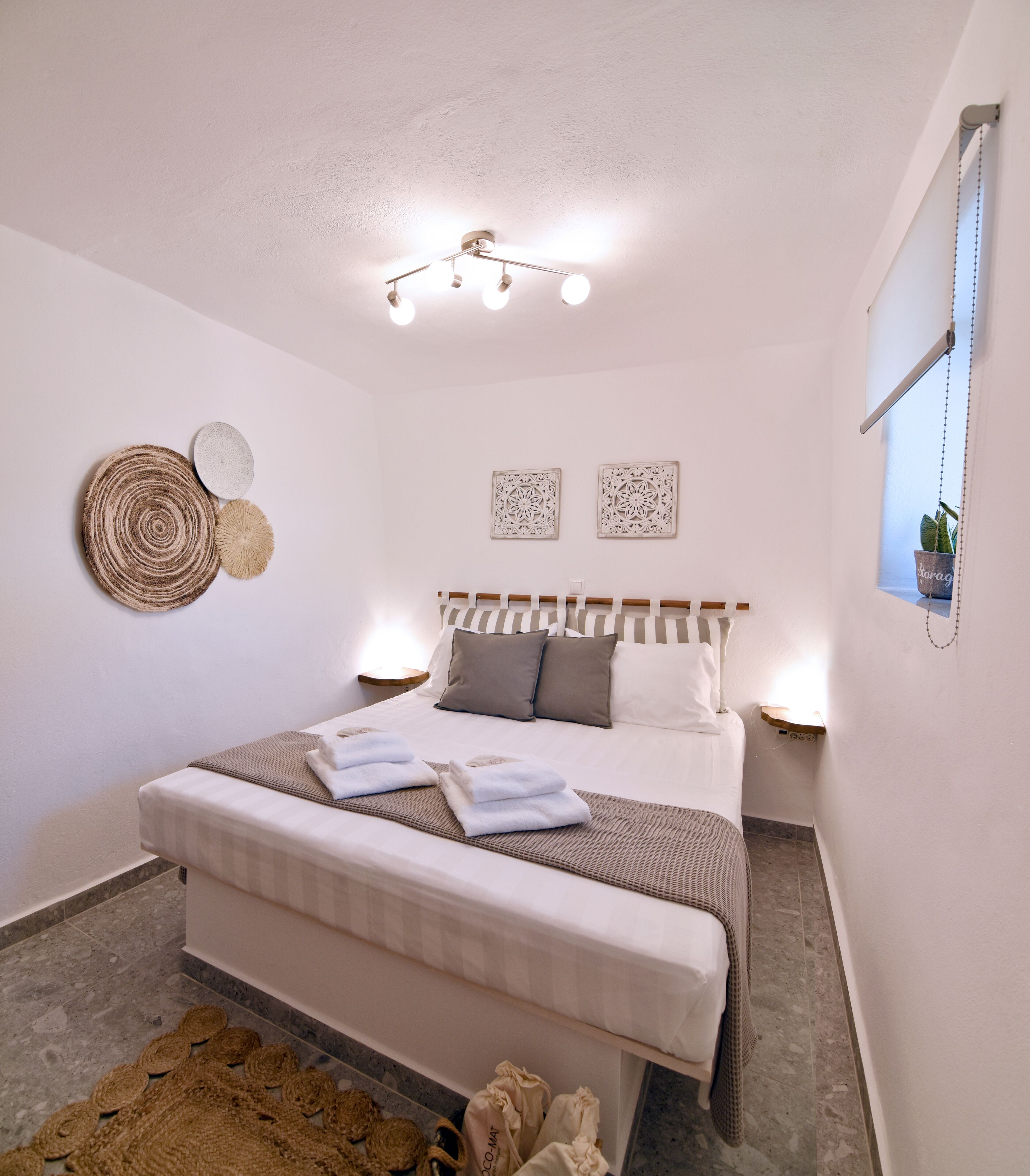 A neatly arranged bedroom with a large bed, bedside lamps, decorative wall art, and a hanging plant.