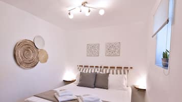 A neatly arranged bedroom with a large bed, bedside lamps, decorative wall art, and a hanging plant.