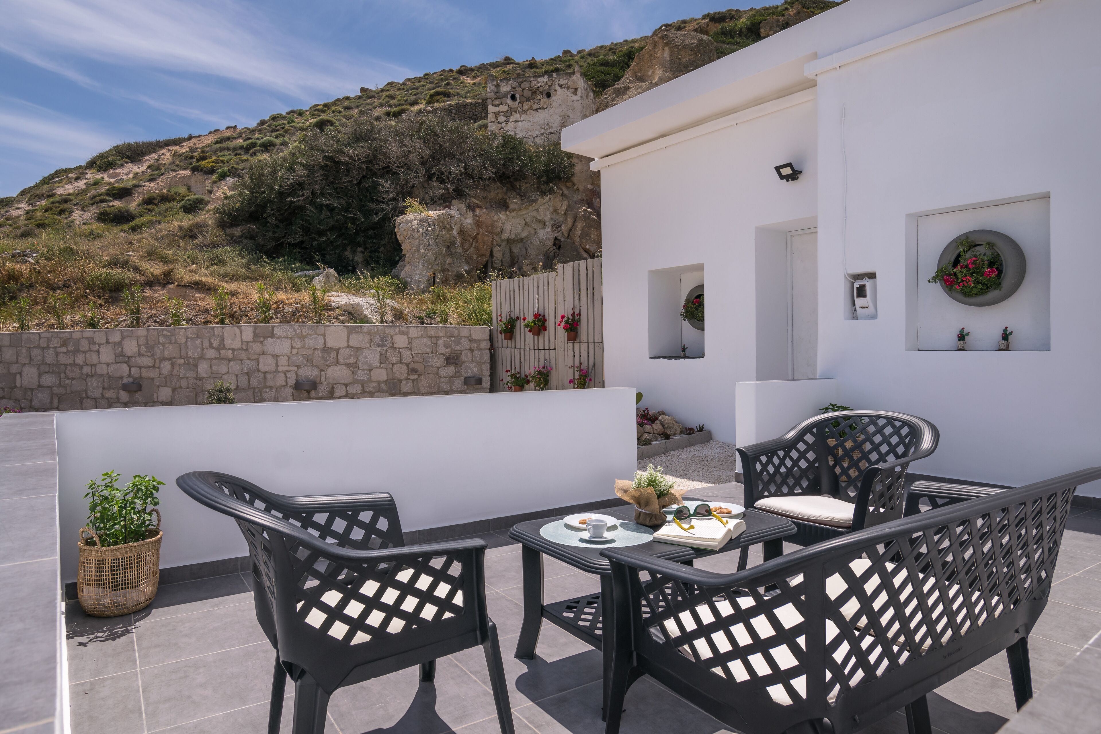 A terrace with a table and chairs, a potted plant, and a view of a rocky hillside.