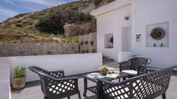 A terrace with a table and chairs, a potted plant, and a view of a rocky hillside.