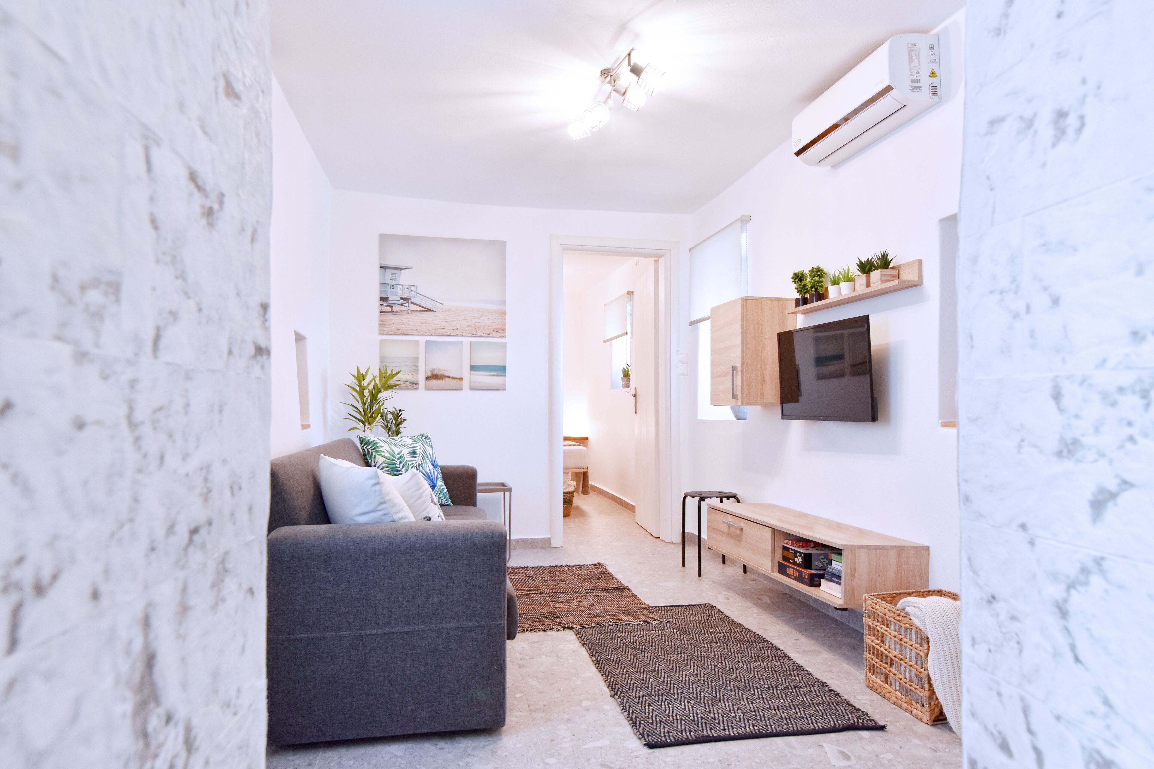 A modern living room with a grey sofa, a flat-screen TV mounted on the wall, a wooden console table, and a small wooden bench.