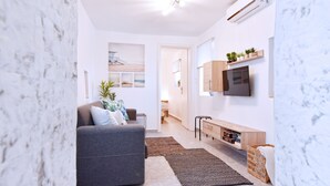 En moderne stue med en grå sofa, et fladskærms-tv monteret på væggen, et træsofabord og en lille træbænk.