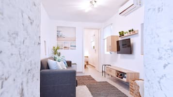 A modern living room with a grey sofa, a flat-screen TV mounted on the wall, a wooden console table, and a small wooden bench.