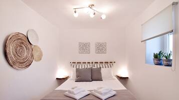 Un lit bien fait, avec deux oreillers, une table de chevet avec une lampe, et des éléments de décoration murale comprenant un objet tissé de forme circulaire et deux motifs encadrés.