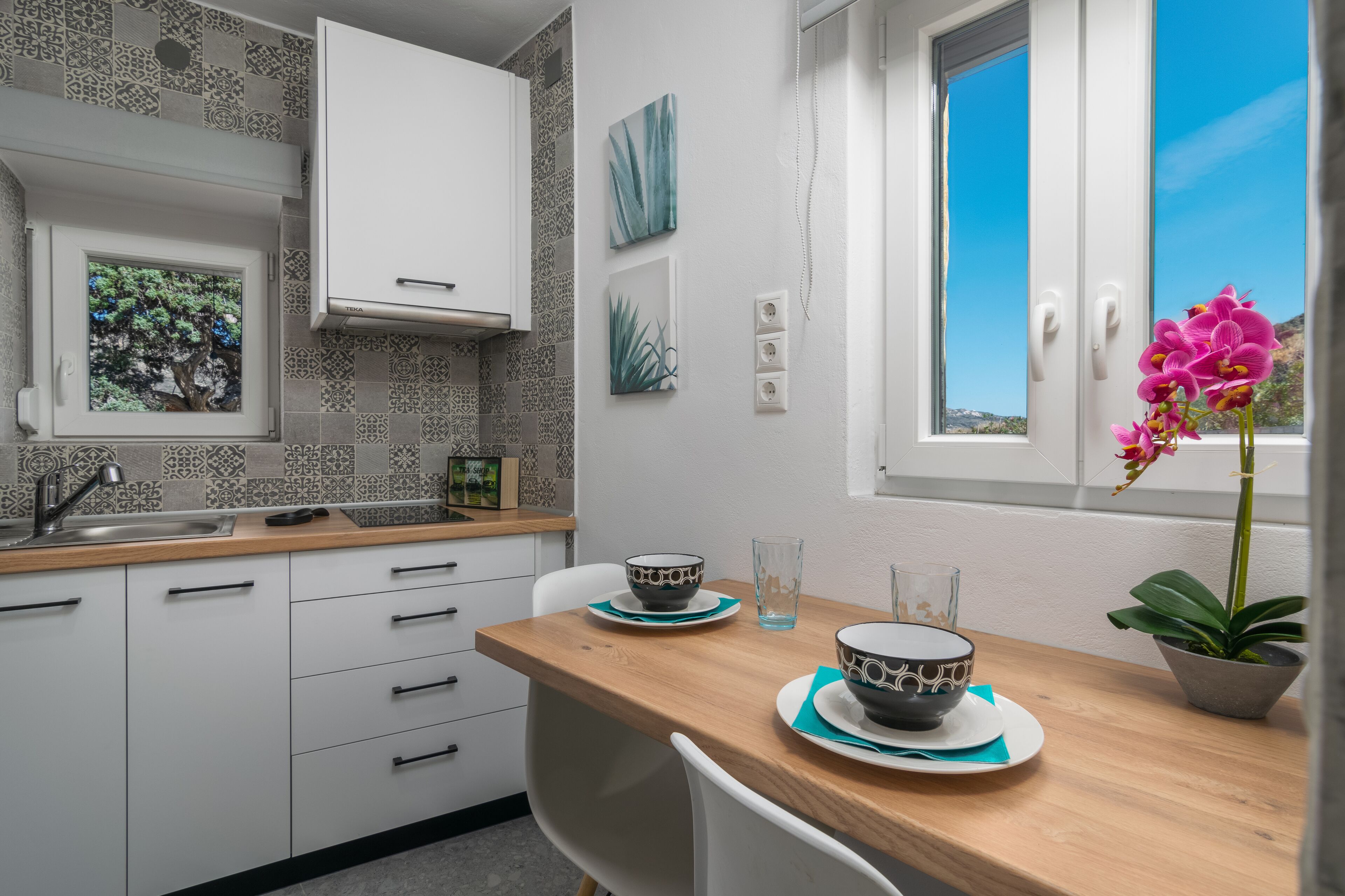 A modern kitchen with white cabinets, a wooden countertop, and a window with a view of the sky.
