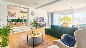 Una sala de estar moderna con un sofá verde, una mesa de centro con un juego de ajedrez y un comedor con sillas verdes y un cuadro.