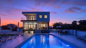 Una casa moderna de dos pisos con piscina, mobiliario exterior y balcón.