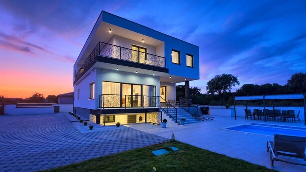 Una casa moderna de dos pisos con balcón, piscina y césped cuidado.