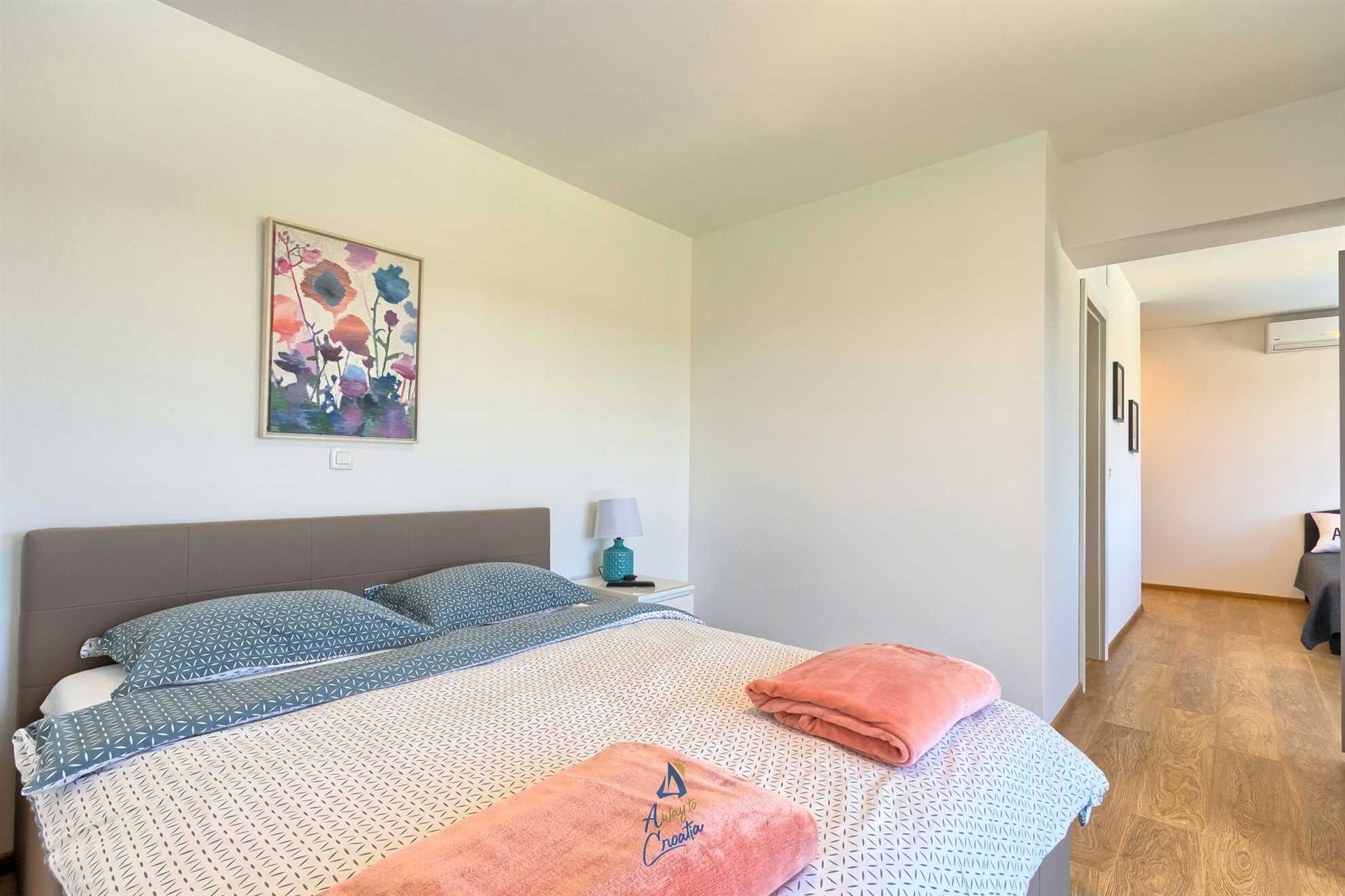 A bedroom with a bed, pillows, a nightstand, a lamp, and a painting on the wall.