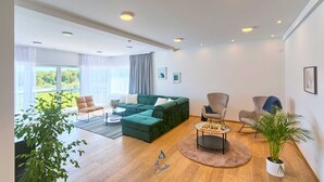Amplia sala de estar con un sofá verde, una mesita de centro y vistas al exterior con vegetación.