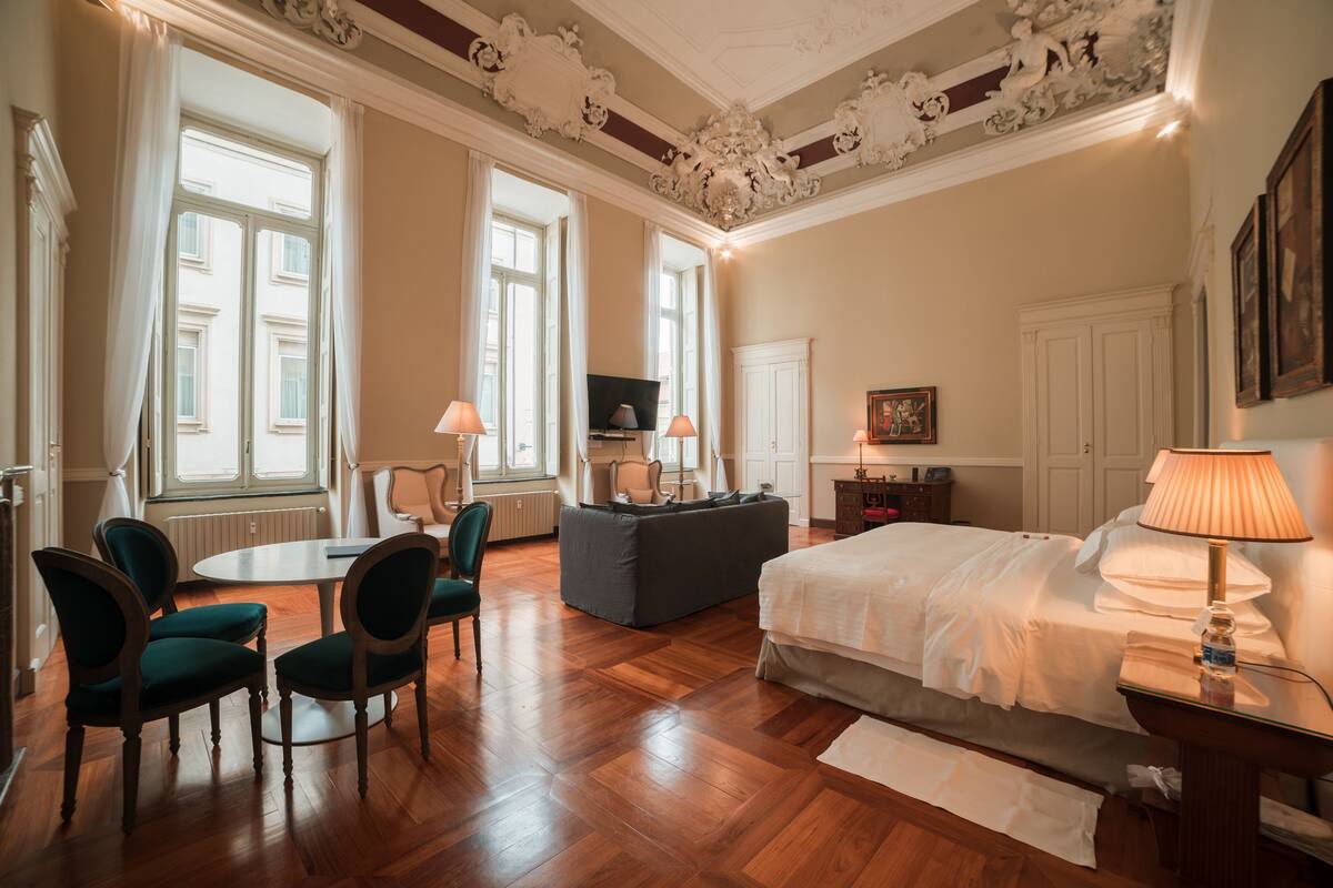 A spacious hotel room with a large bed, a dining table with chairs, a sofa, and a television.