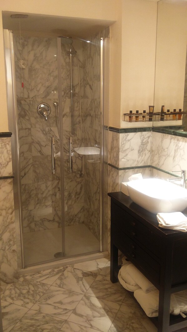 A bathroom with a glass-enclosed shower, a marble-tiled floor, a glass sink, and a dark wooden vanity. - Royal Palace Luxury Suites & Hotel (Turin)