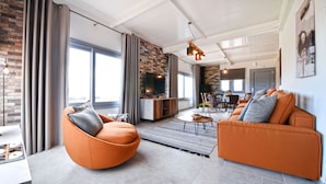 A modern living room with a large window, a fireplace, and a dining area in the background. - Nino's Country House (Milos)