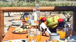 A wooden table set with breakfast items, including fruits, pastries, and beverages, overlooking a scenic landscape. - Nino's Country House (Milos)