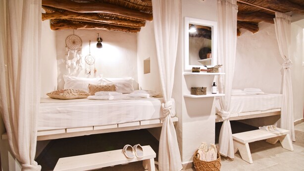 A bedroom with two beds, a bench, a bedside table, a mirror, and a basket. - Nino's Country House (Milos)