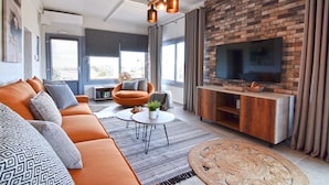 A modern living room with a brick wall, a large flat-screen TV, a sofa, a coffee table, and a patterned rug. - Nino's Country House (Milos)