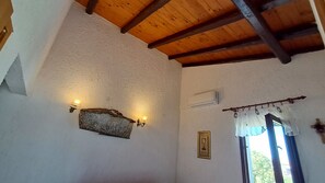 A room with a sloped ceiling, a wall-mounted air conditioner, a window with curtains, and a framed picture.