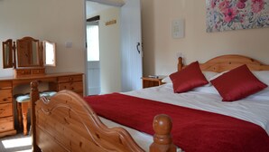 A bedroom with a wooden bed, red pillows, a red throw blanket, a wooden dresser, and a mirror. - Converted barn, with hot tub near to North Devon's beaches (Barnstaple)