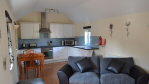 A compact living space with a kitchenette, a dining area, and a sofa. - Converted barn, with hot tub near to North Devon's beaches (Barnstaple)