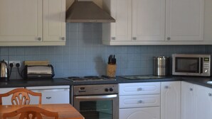 A kitchen with white cabinets, a stove, a microwave, and a toaster. - Converted barn, with hot tub near to North Devon's beaches (Barnstaple)