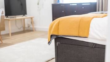 A bedroom with a bed, a TV on a stand, a desk, and a wardrobe.