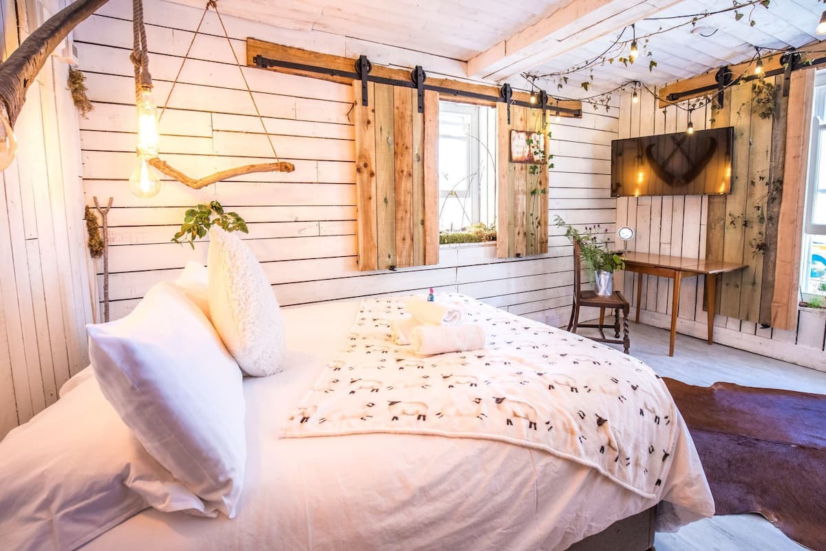 A cozy bedroom with a bed, a hanging light, a wooden wall, and a TV.